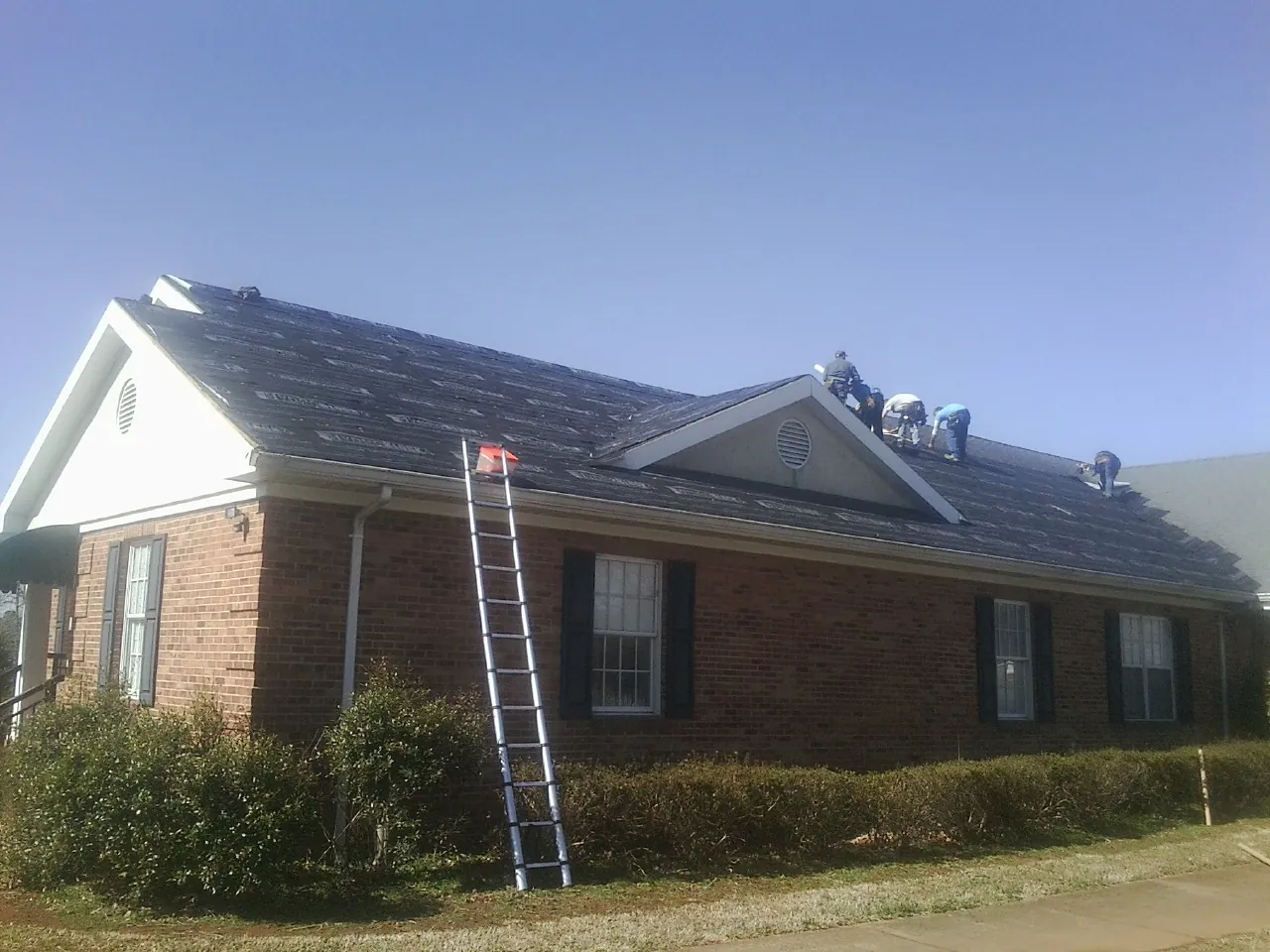 Crew tearing shingles off a brick ranch roof with a ladder set — Emergency Roof Repair work by our crew in Sterling