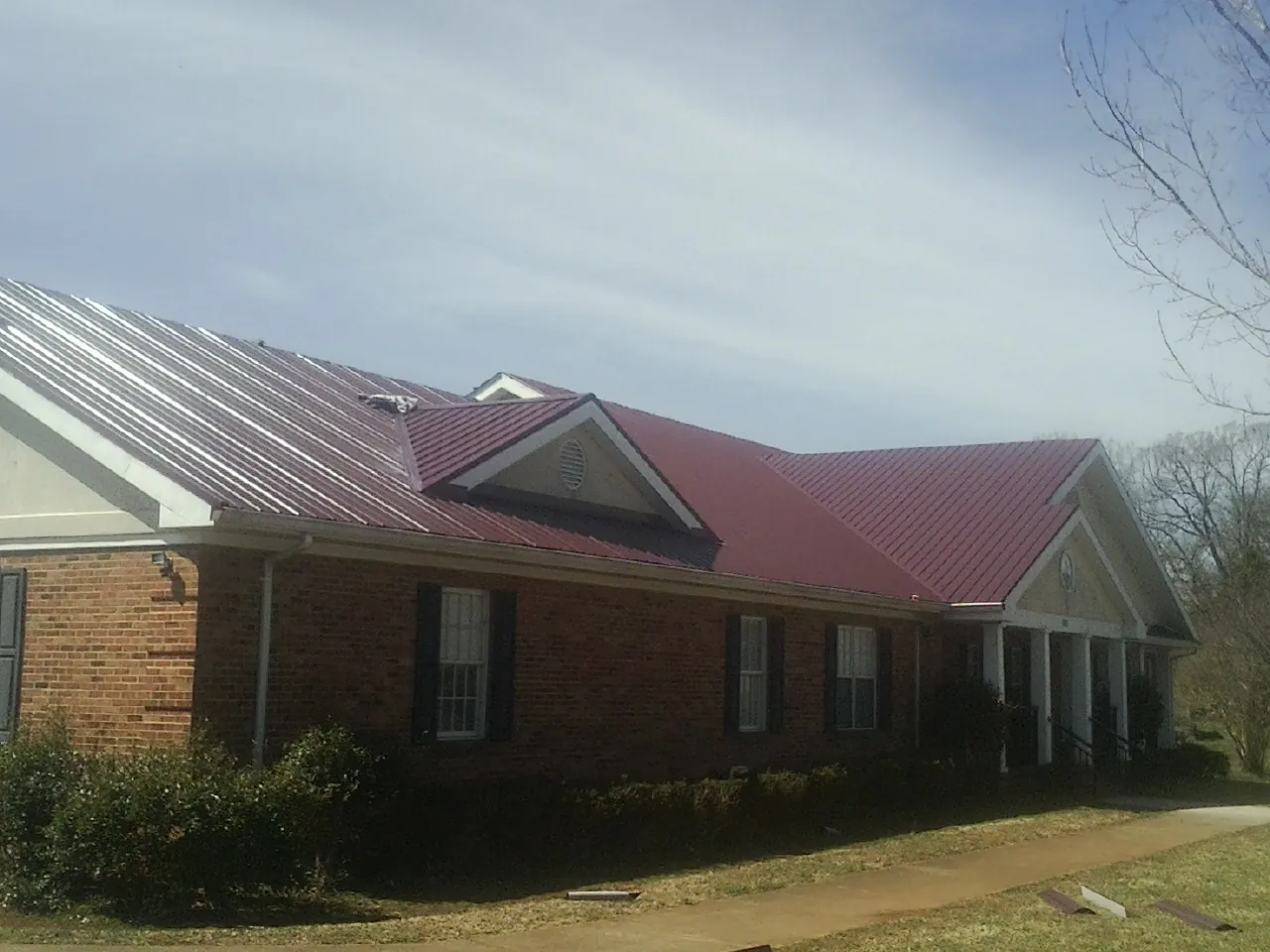 Red metal roof with gabled entries on a long brick building, from a Hail Damage Roof Repair job in Sterling
